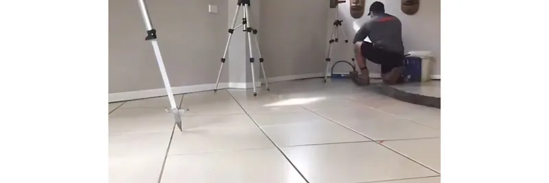 Worker with laser tripods injecting resin through tiled floor