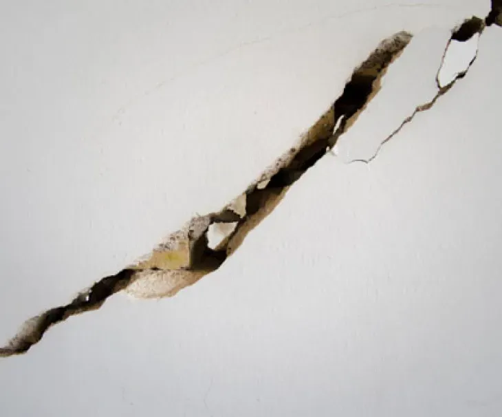 Deep diagonal wall crack with masonry fully separated showing daylight through