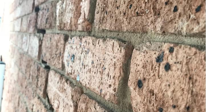 Weathered red brick wall showing rising damp and mortar deterioration issues.
