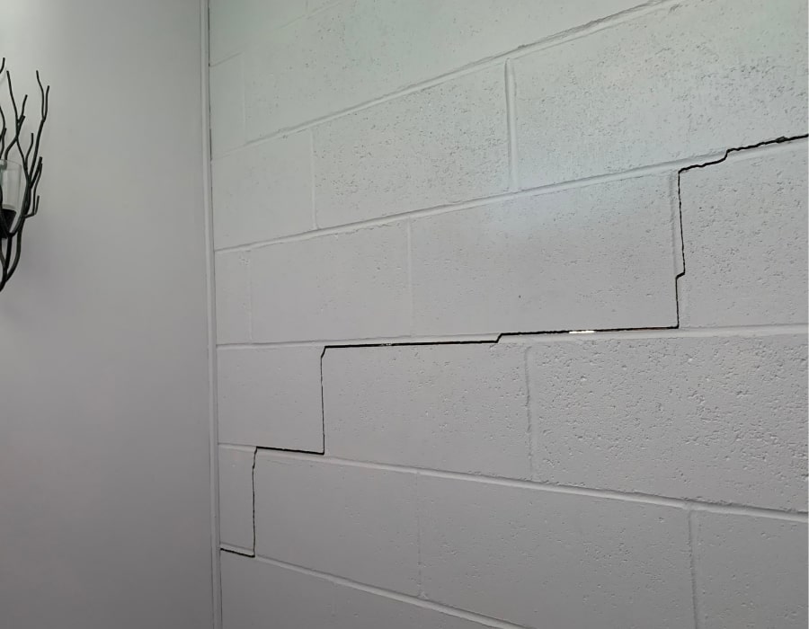White cinderblock wall with horizontal zigzag cracks indicating subsidence and foundation repair need.