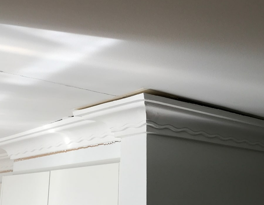 Misaligned crown molding and ceiling gap suggest foundation subsidence and wall cracks.
