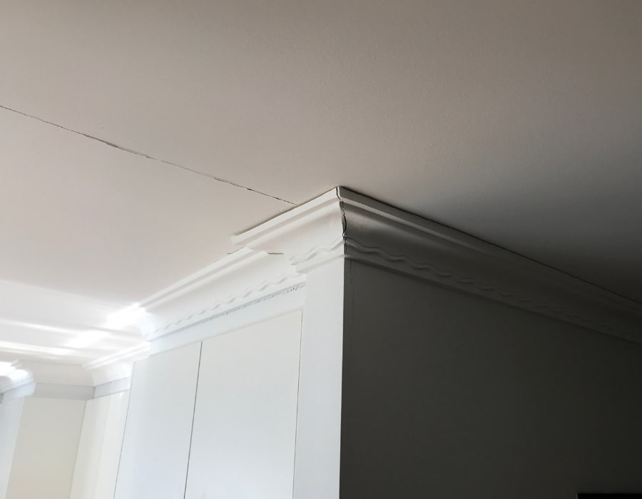 Ceiling crack near crown moulding indicating subsidence and potential foundation repair.