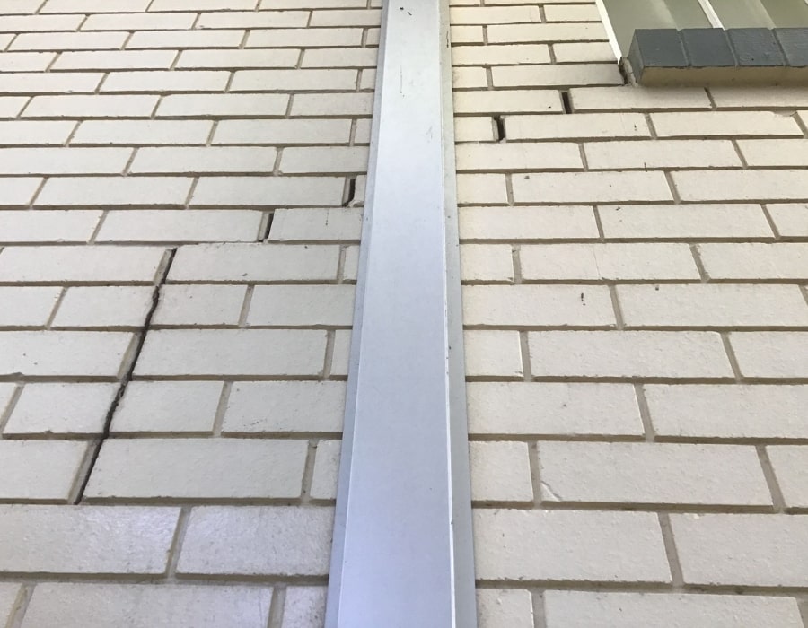 White brick wall with subsidence cracks, vertical steel reinforcement, and rising damp.