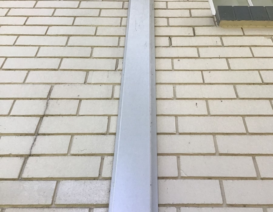 Vertical metal conduit installed on cracked brick wall showing subsidence issues.