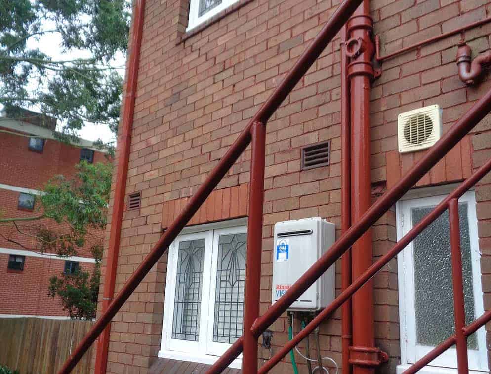 Red bracing poles stabilise brick wall foundation repair near rising damp area.
