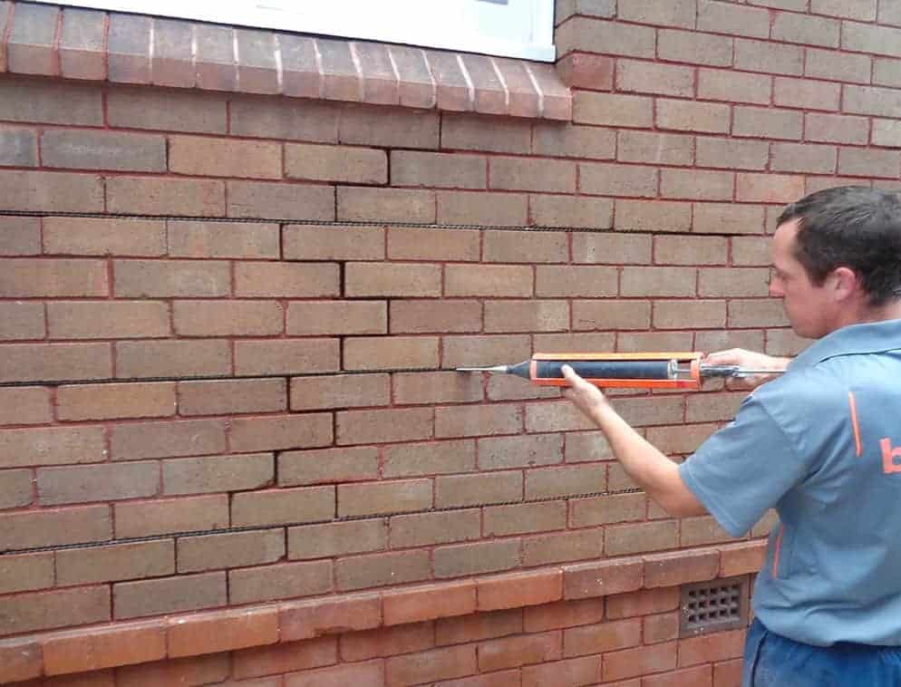 Technician injecting sealant into brick wall cracks to prevent rising damp.