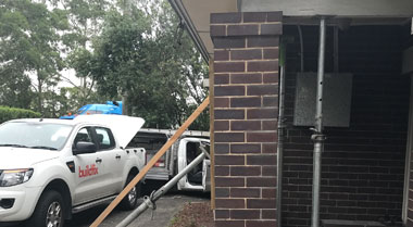 Brick house corner stabilised with timber props for foundation subsidence repair works.