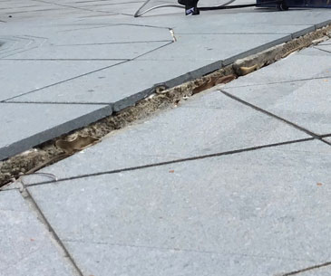 Uneven cracked sidewalk tiles showing subsidence and foundation repair needs.