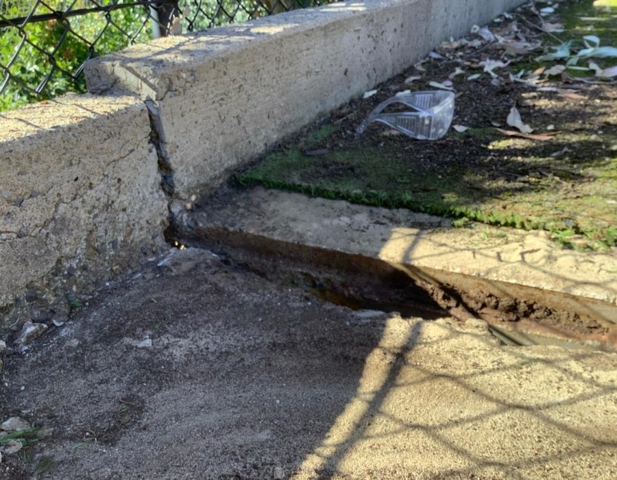 Concrete curb subsidence with foundation crack exposing soil and rising damp.