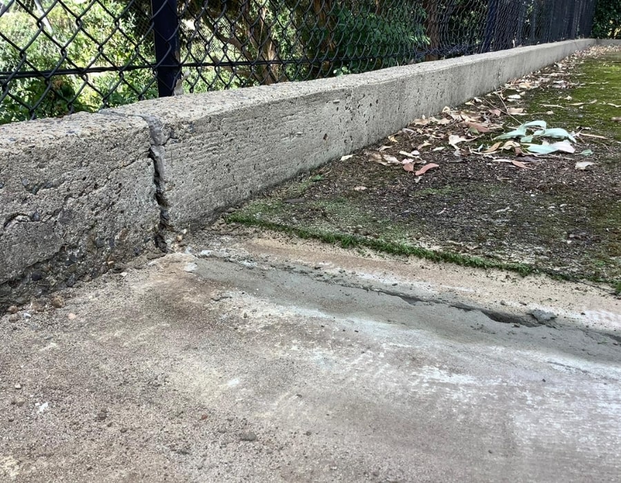 Cracked concrete kerb with subsidence and moss indicating foundation movement.