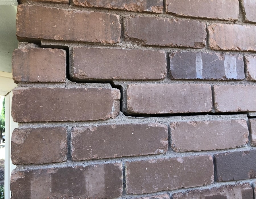 Brick wall with horizontal and stair-step cracks indicating subsidence and foundation repair needs.