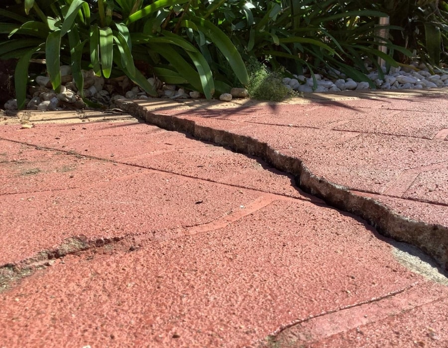 Large crack in red brick patio indicates subsidence and foundation repair needs.