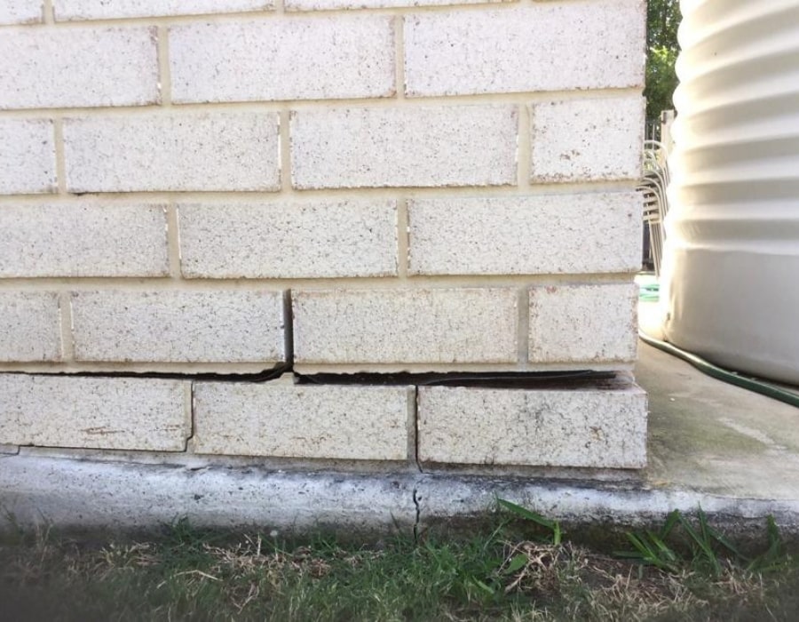 Horizontal brick wall crack and subsidence above foundation, indicating structural repair needed.