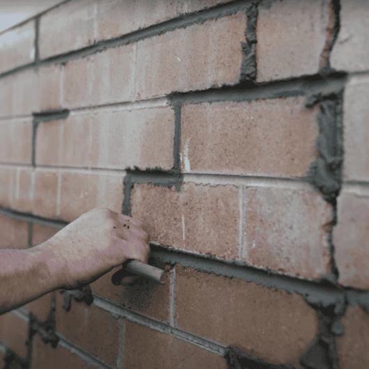 Hand applying mortar between bricks for wall crack repair and stabilisation.