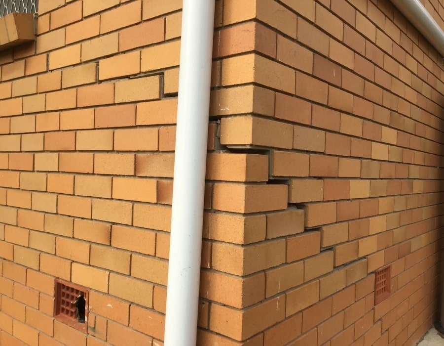 Uneven brick wall corner with shifted bricks indicating foundation subsidence and wall cracks.
