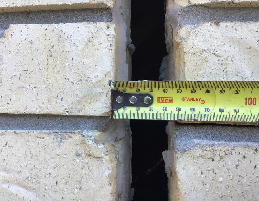 Measuring tape assessing wide vertical wall crack indicating subsidence and foundation repair.