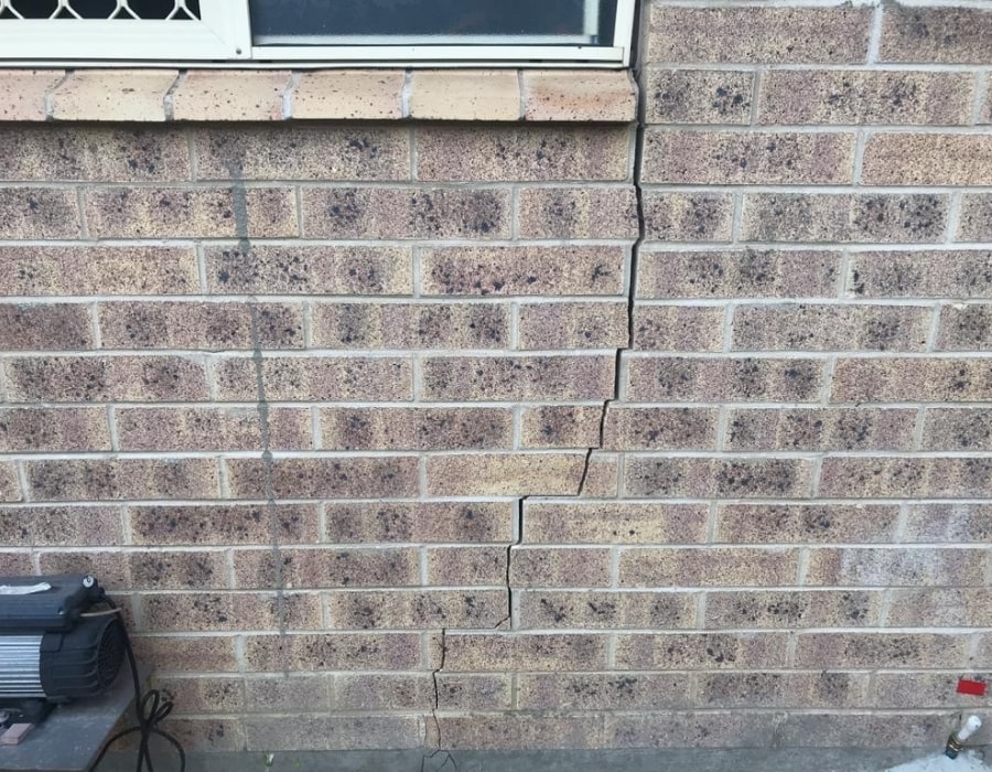 Large vertical wall crack assessed for subsidence and foundation repair with device.
