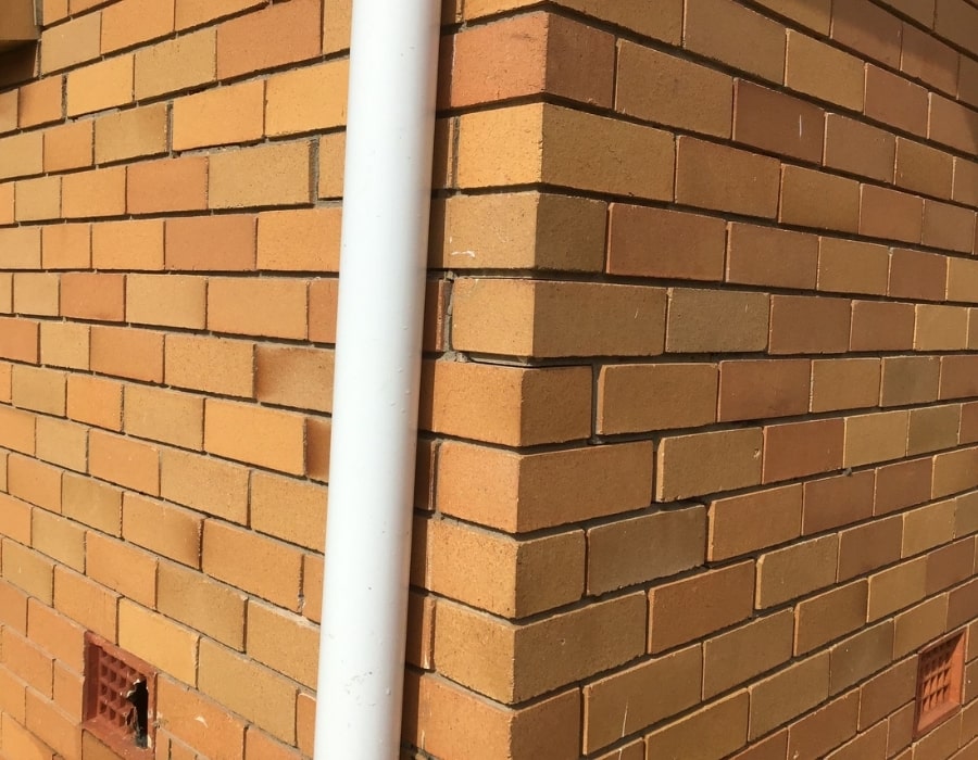 Brick building corner with subsidence signs and ventilation grates, foundation repair needed.