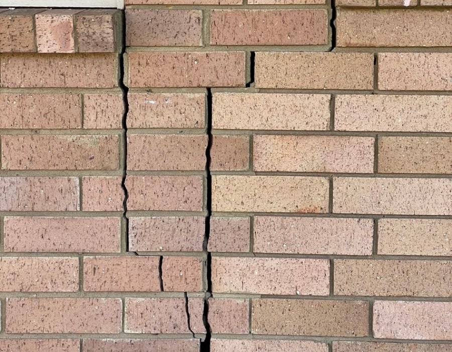 Vertical crack in brick wall indicating foundation subsidence and structural repair needs.