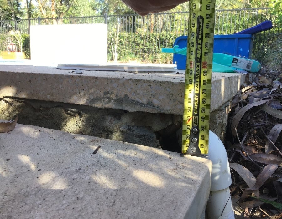Measuring foundation subsidence at stone pool edge with visible wall crack.