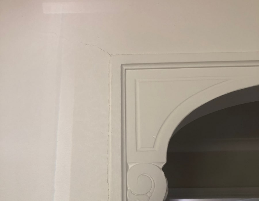 Cream wall crack near arched doorway indicates subsidence and foundation repair need.