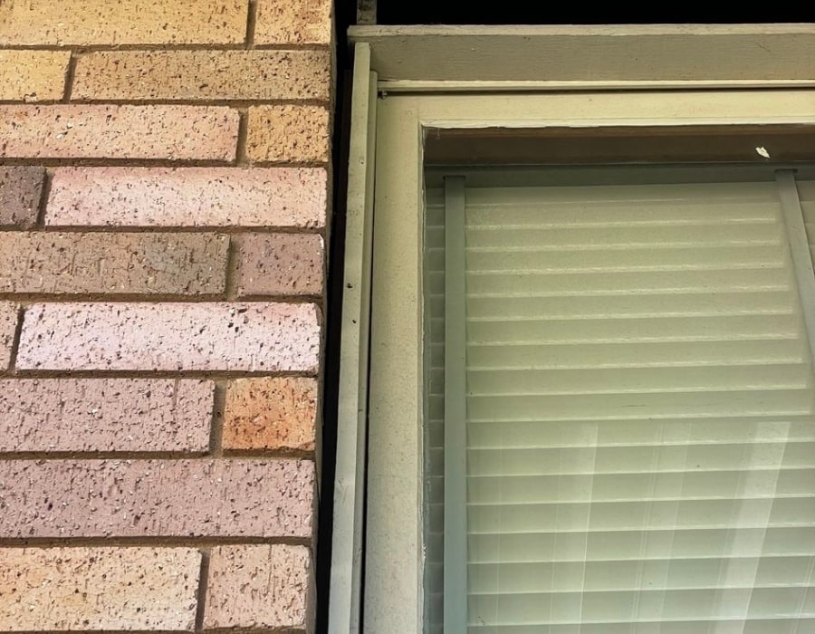 Brick wall with window frame junction inspected for foundation subsidence cracks.