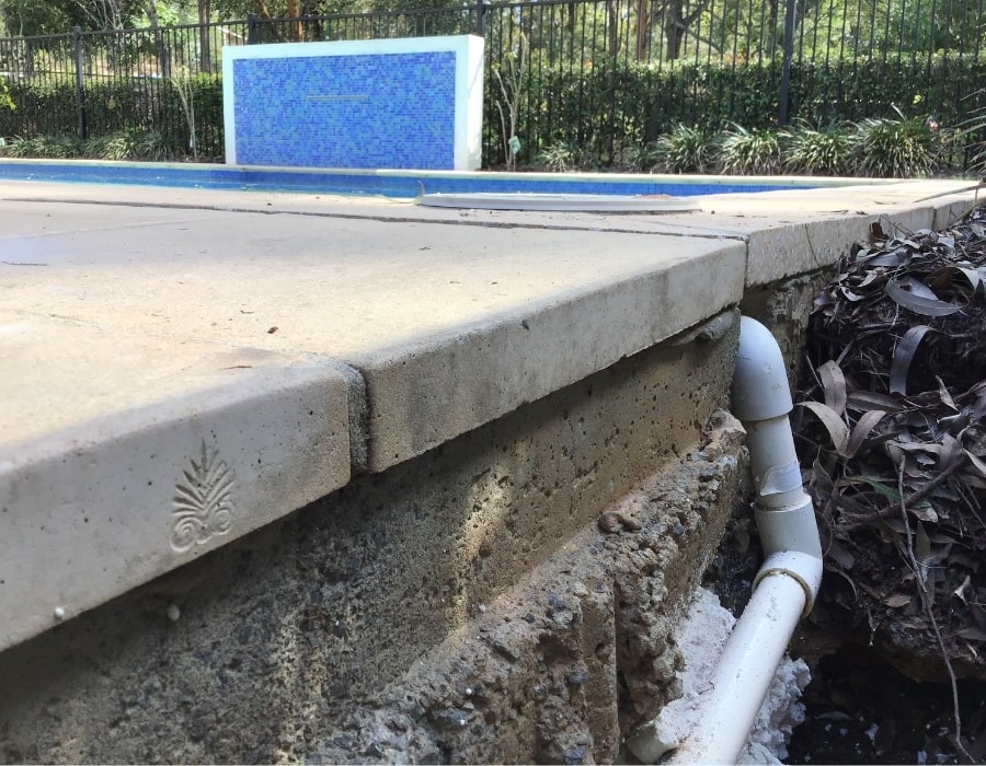 Exposed pool drainage pipe and eroded concrete edge indicating subsidence risk.