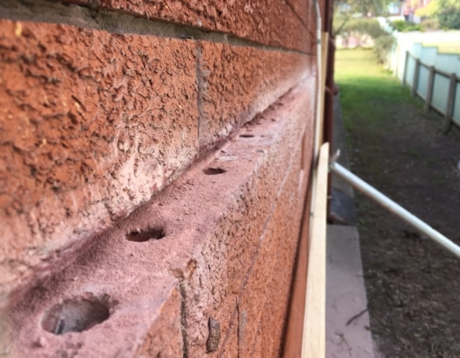 Red brick wall with wall cracks, underpinning holes for foundation repair.