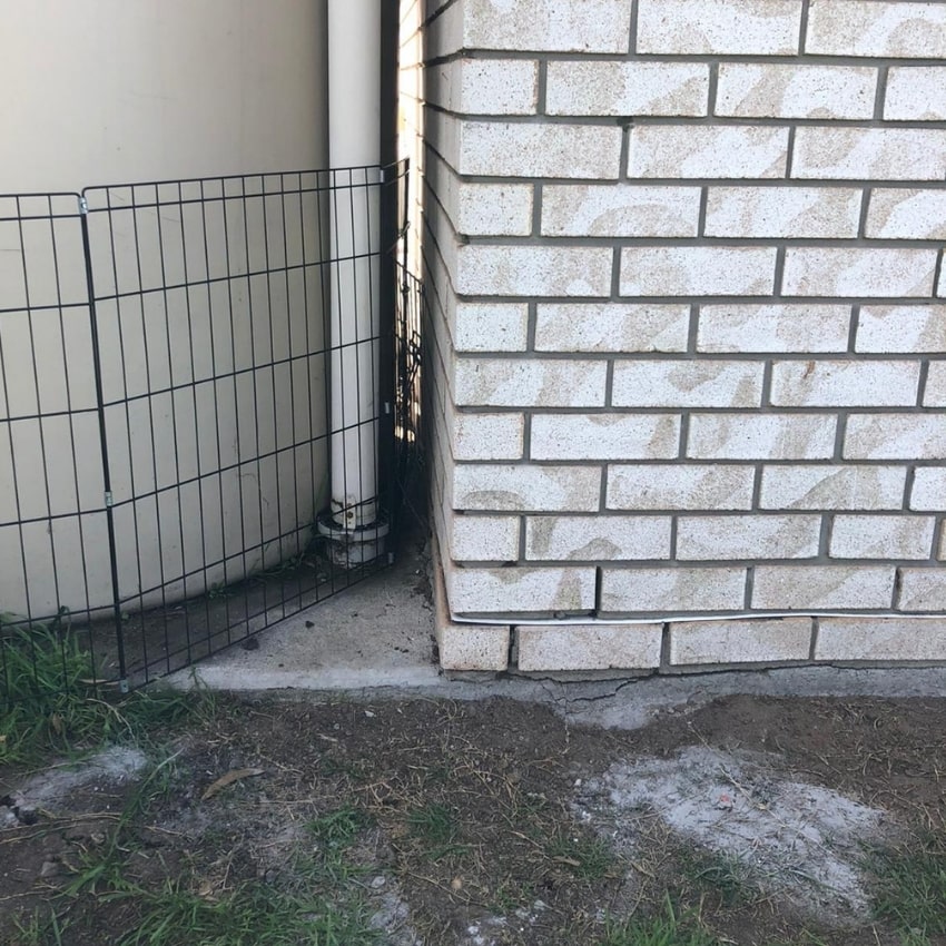 Wire fence beside water tank highlights potential foundation subsidence and structural repair needs.