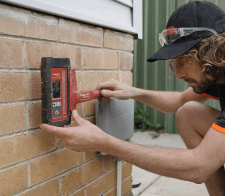Technician inspecting brick wall for foundation cracks using electronic moisture meter.