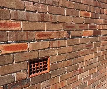 Brown brick wall with horizontal lines indicating rising damp and vent opening.