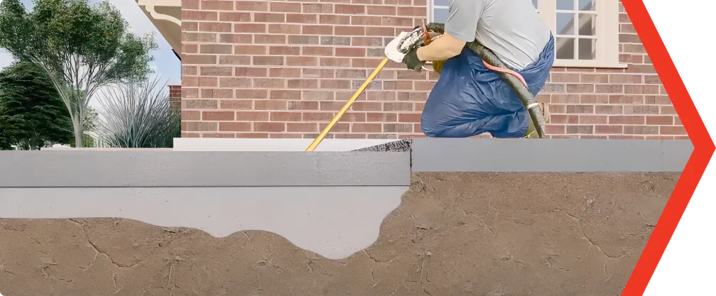 Worker applies waterproofing membrane to brick house foundation for rising damp prevention.