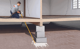 Worker injects GeoPoly material under house for foundation subsidence repair.