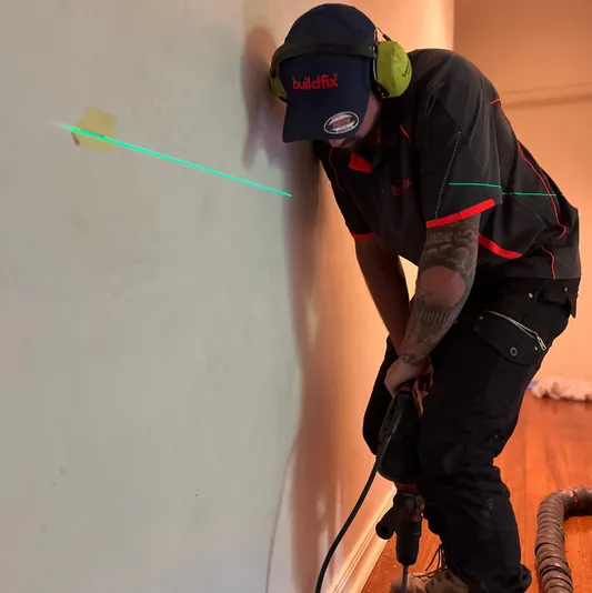 Worker drilling near floor with laser level for foundation repair solution.