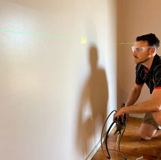 Technician uses power tool to stabilise wall cracks with laser alignment.