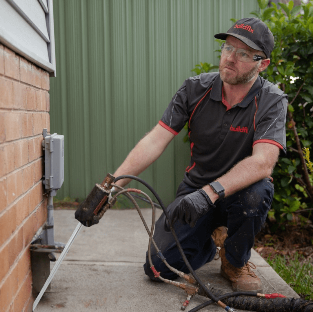 Buildfix technician injecting GeoPoly resin for foundation repair below cracked brick wall.